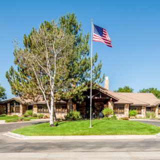 A residential house with a US flag flying in the front yard, surrounded by trees and a well-maintained lawn.