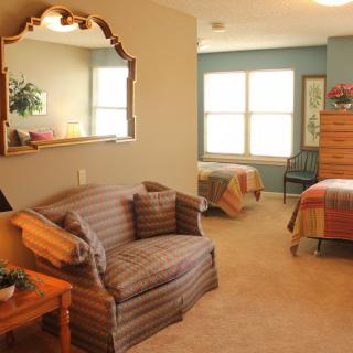 A cozy bedroom with twin beds, a sofa, and a large mirror reflecting natural light from the window.