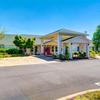 A building entrance with a covered driveway and landscaped surroundings under a clear blue sky.