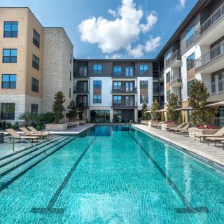 A luxury apartment complex with a pristine outdoor swimming pool under a clear blue sky.