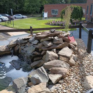 A serene waterfall feature surrounded by rocks and pebbles, with greenery in the background.