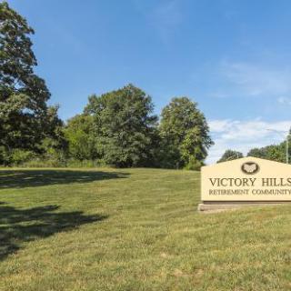A welcoming sign for Victory Hill, set against a backdrop of lush greenery and clear blue skies.