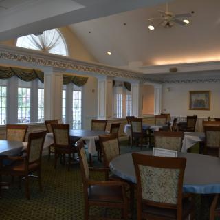 An empty dining room with multiple tables and chairs, featuring large windows.