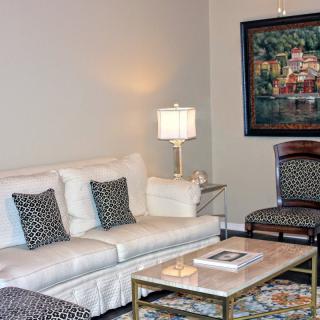 A cozy living room with a white sofa, patterned pillows, a coffee table, and a lamp next to framed artwork on the wall.