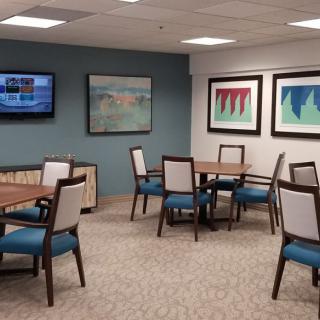 A well-lit room with several tables and chairs, decorated with colorful artwork and a wall-mounted TV.
