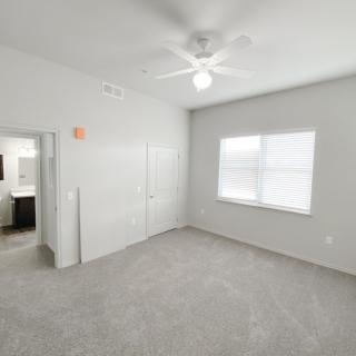 A bright, empty bedroom with a ceiling fan and carpet flooring.