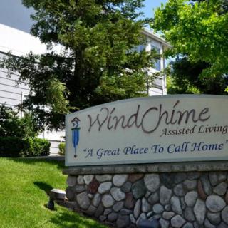 Sign for WindChime Assisted Living with a building and lush greenery in the background.