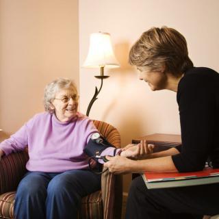 A healthcare professional checking an elderly woman's blood pressure during a home visit.