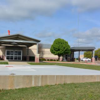 A modern school building surrounded by green grass and trees under a partly cloudy sky.