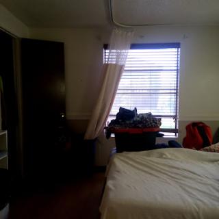 A cozy bedroom featuring a bed, window with curtains, and a wooden door.