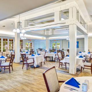 A bright and elegant restaurant dining area with neatly arranged tables and chairs, featuring blue napkins and a wooden floor.