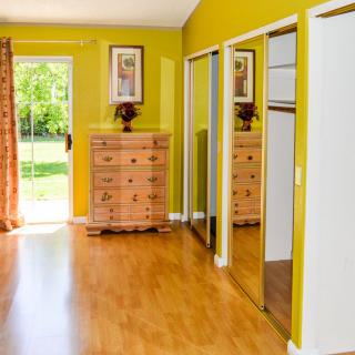 A bright bedroom with yellow walls, wood flooring, a dresser, and mirrored closet doors.