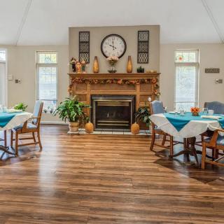 A cozy dining area with a central fireplace, surrounded by tables and chairs, featuring decorative elements and indoor plants.