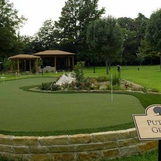 A beautifully landscaped putting green surrounded by trees and garden elements.