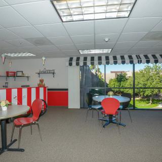 A spacious office breakroom with red and black furniture and large windows providing natural light.