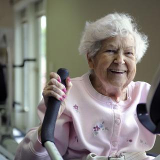 An elderly woman smiling while using exercise equipment.