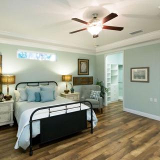 A modern bedroom with a stylish metal bed frame, cozy armchair, ceiling fan, and hardwood flooring.