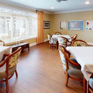 A cozy dining area with several tables and chairs, featuring large windows and wall decorations.