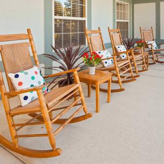 A row of wooden rocking chairs with colorful cushions on a porch.