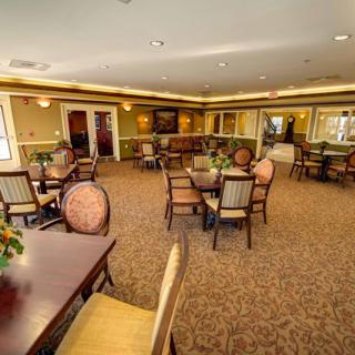 A spacious dining area with multiple tables and chairs, featuring carpeted flooring and decorative lighting.