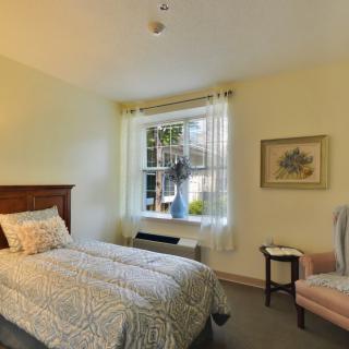 A cozy bedroom with a single bed, armchair, and a window letting in natural light.
