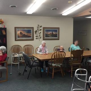 A group of elderly people seated around a table in a nursing home.