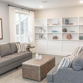A modern living room with neutral tones featuring two gray sofas, a central table, and a large white bookshelf.