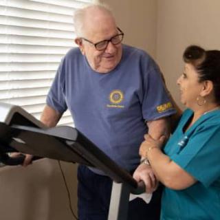 An elderly man receives assistance from a healthcare professional while exercising on a treadmill.