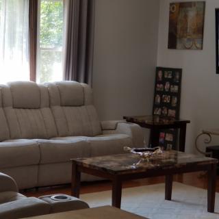 A cozy living room with a beige sofa and wooden coffee table, adorned with artwork and natural light streaming through the windows.