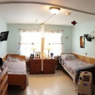 A shared hospital room with two beds, side tables, and medical equipment by the window.