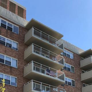 A multi-story apartment building with balconies and a brick exterior under a clear blue sky.