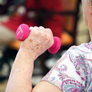 A senior person exercising with a pink dumbbell.