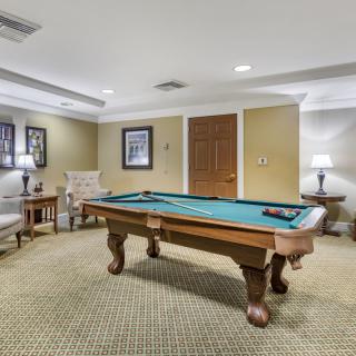 A cozy recreational room featuring a pool table at the center, surrounded by elegant furnishings and soft lighting.