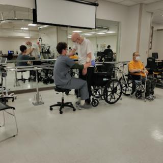 A therapy session in a rehabilitation center with patients using wheelchairs and healthcare professionals assisting.