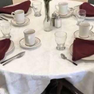 A formal dining table set with white cloth, burgundy napkins, and elegant dinnerware.