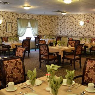 A cozy dining room with elegantly set tables and floral wallpaper.