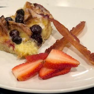 A slice of berry-topped cake served with fresh strawberries on a white plate.