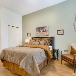 A cozy bedroom featuring a bed with neutral bedding, accompanied by a chair and decorative wall art.
