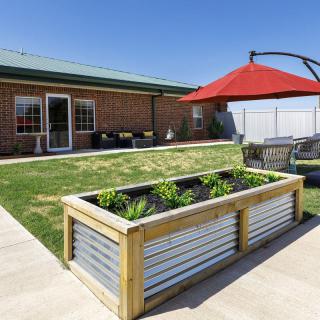 A backyard garden with a raised bed and a red umbrella on the patio.