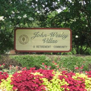 A sign for John Wesley Villas, a retirement community, surrounded by a landscaped garden with colorful flowers.