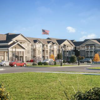 A residential building complex with well-maintained landscaping and an American flag displayed in front, under a clear blue sky.
