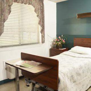 A simple hospital room with a bed, bedside table, and curtain-covered window.