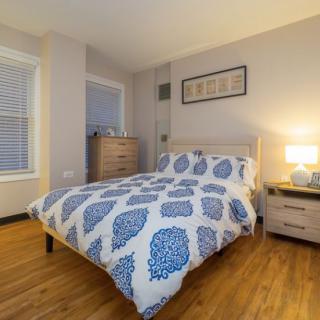 A cozy bedroom with a neatly made bed featuring a blue and white patterned duvet, complementing wooden furniture, and soft lighting.