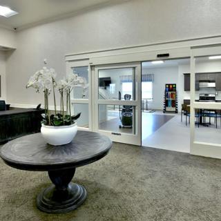 The image depicts a modern lobby entrance with a decorative table and flower pot.