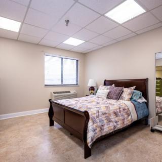 A cozy bedroom with a wooden bed, decorative pillows, a mirror, and natural light coming through the window.