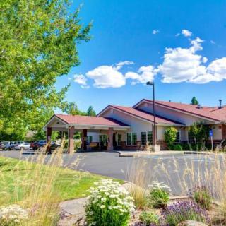 A scenic view of a building with a red roof surrounded by trees and shrubs under a bright blue sky with clouds.