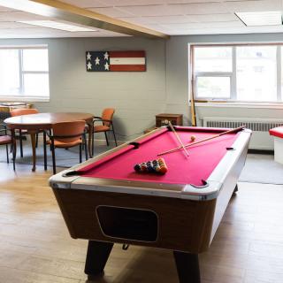 A game room featuring a pool table with red felt and seating area.