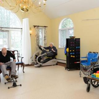 Elderly individuals engaging in exercise activities in a therapy room equipped with fitness machines.