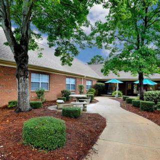 A neatly landscaped courtyard with a brick building, trees, and outdoor seating under blue umbrellas.