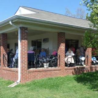 A group of people sitting on a porch with wheelchairs on a sunny day.